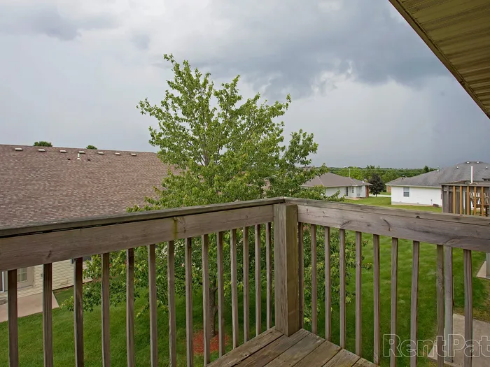 Private wooden balcony at Huntley Ridge Apartments overlooking nearby rooftops and green lawns, perfect for relaxing with a view.