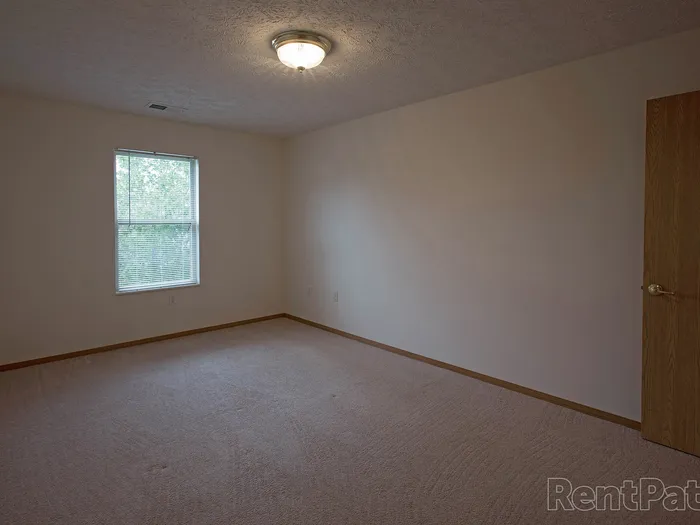 Roomy bedroom with neutral walls, soft carpeting, and a single window bringing in natural light.