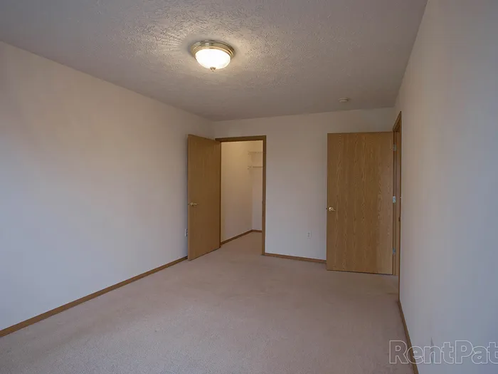 Open layout bedroom with two wooden doors&mdash;one leading to the hallway and the other to a closet&mdash;ideal for a comfortable sleeping space.