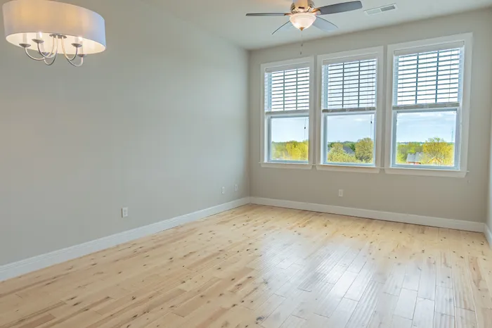 Open living space at Chesterfield Lofts in Springfield, MO, featuring hardwood flooring, large windows with scenic views, and a modern ceiling fan with a light fixture. This versatile area is perfect for creating a stylish and comfortable home in this luxury apartment community.