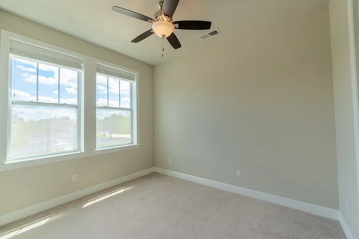 Spacious bedroom at Chesterfield Lofts with large windows letting in natural light, light gray walls, soft carpet flooring, and a ceiling fan. A modern and neutral space ideal for relaxation.