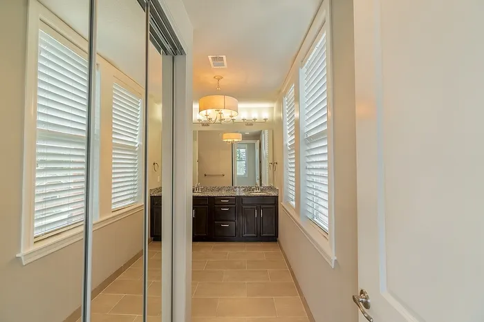 Spacious hallway at Chesterfield Lofts with mirrored closet doors, large windows with blinds, and a modern bathroom featuring a granite vanity and dark cabinetry.