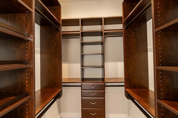 Luxury walk-in closet at Chesterfield Lofts featuring built-in dark wood shelving, drawers, and multiple hanging rods for optimized storage and organization.