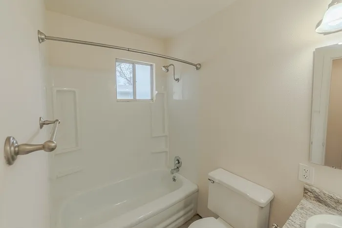 Bathroom at Village Club Apartments Springfield MO featuring a white tub with shower, built-in shelving, and a frosted window above the tub. Towel bars are mounted on the wall.