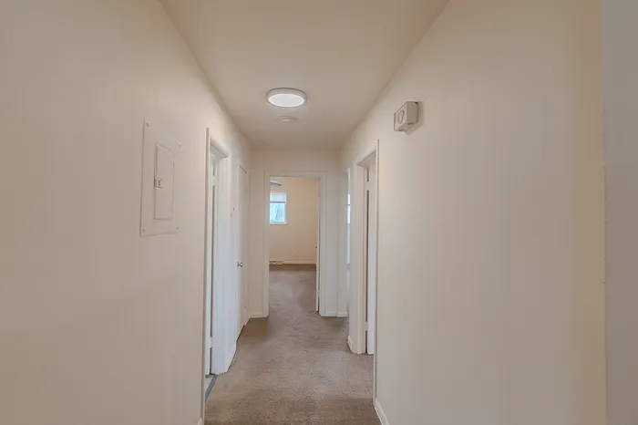 Interior hallway at Village Club Apartments Springfield MO with beige carpet, neutral walls, overhead flush light, and doorways to bedrooms and bathroom on both sides.