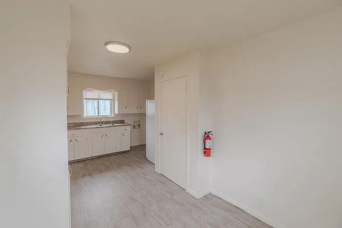 Reverse view of the kitchen at Village Club Apartments Springfield MO showing full sink and cabinet area, refrigerator, and storage closet with fire extinguisher mounted on the wall, maintaining accessibility and safety for affordable housing units.