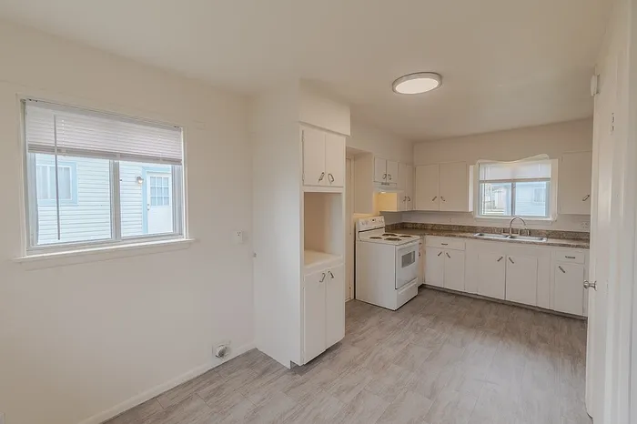 Kitchen and dining area in a Village Club Apartment in Springfield MO with large window, open wall cabinet, white electric stove, and ample countertop space for affordable and functional living.