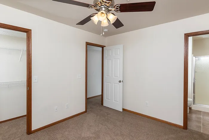 Carpeted bedroom at Lakewood Village featuring a ceiling fan, access to a walk-in closet with built-in wire shelving, and an ensuite bathroom with a walk-in shower.