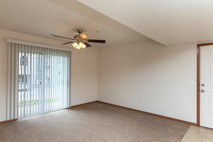Cozy living room featuring a ceiling fan and vertical blinds over a sliding glass door, offering direct access to outdoor space and ample natural light.