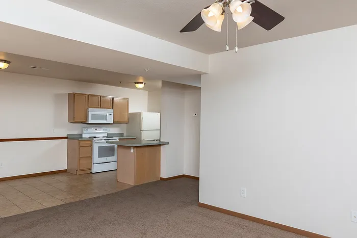 Spacious carpeted living room connected to the kitchen with tile flooring, ideal for entertaining or open-concept living at Lakewood Village Apartments.