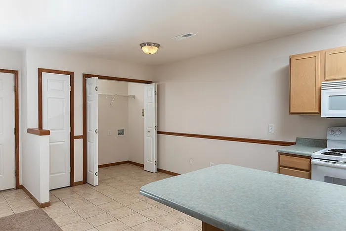View of the open kitchen with light wood cabinetry, tile floors, and adjacent laundry nook with washer and dryer hookups and shelving.