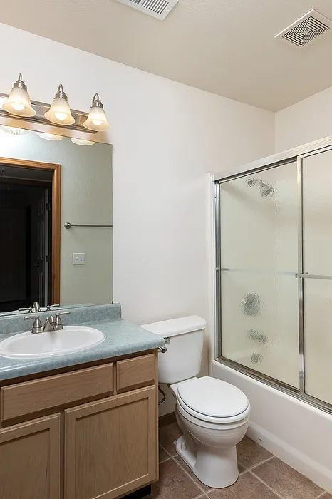 Modern bathroom with tile flooring, single-sink vanity with mirror and light fixture, and a clear glass walk-in shower at Lakewood Village Apartments.