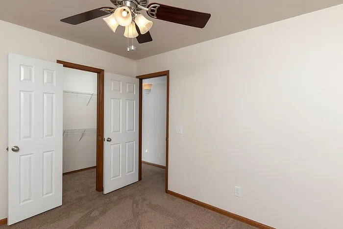 Bedroom with open double-door closet featuring built-in shelving and access to the main hallway, ideal for organization and functionality.