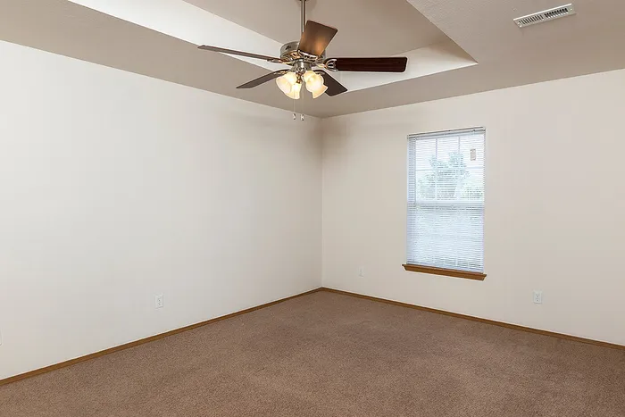 Bright and open bedroom at Lakewood Village featuring neutral carpet, a modern ceiling fan, and natural light from a single wide window.