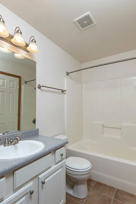 Modern bathroom in Lakewood Village apartment with a white shower-tub combo, single-sink vanity with gray countertop, and overhead lighting above a large mirror.