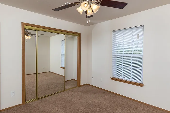 Third bedroom in the Lakewood Village 3-bedroom apartment, highlighted by mirrored sliding closet doors, two large windows for natural light, and a ceiling fan with multiple light fixtures.