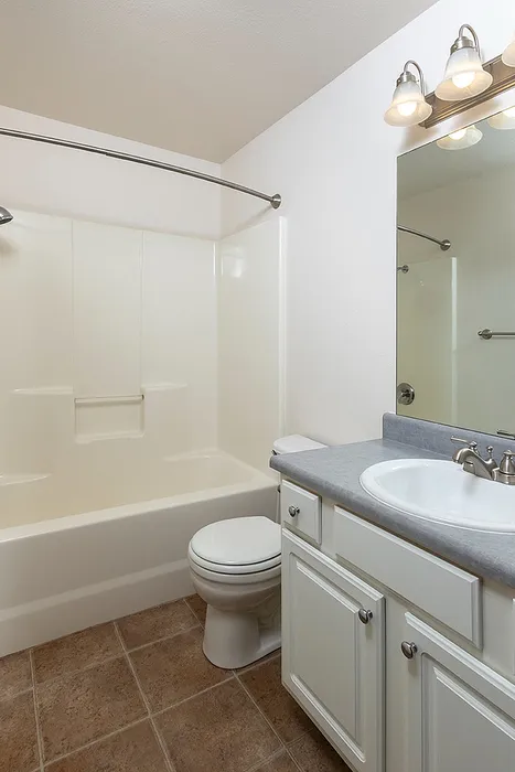 Bright and clean bathroom at Lakewood Village with tiled flooring, spacious vanity, and wall-mounted mirror under soft, brushed-nickel lighting fixtures.