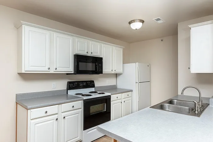 Bright kitchen at Lakewood Village featuring white cabinetry, black appliances, a double stainless steel sink, and light gray countertops.