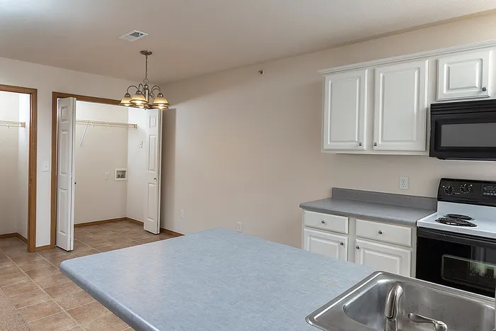 Open view from the kitchen toward a tiled dining space with overhead lighting and a laundry area with washer and dryer hookups at Lakewood Village apartments.
