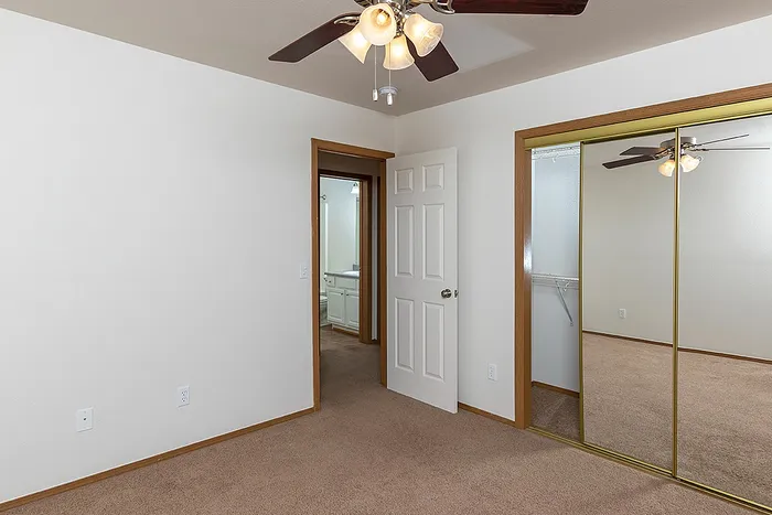 Bedroom with ceiling fan, mirrored closet doors, and direct access to a bathroom at Lakewood Village&rsquo;s spacious 3-bedroom, 2-bath unit.