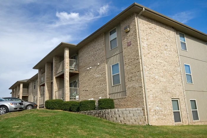 Street-side view of Lakewood Village Apartments in Springfield, MO, showcasing a clean brick exterior, private balconies, well-maintained landscaping, and adjacent parking&mdash;offering comfortable suburban apartment living.