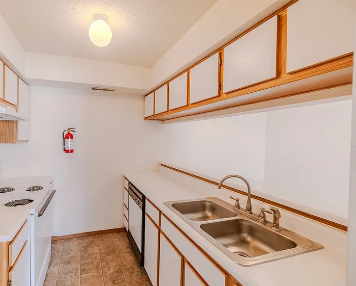 Galley-style kitchen at Huntley Ridge East Apartments in Springfield, MO with ample cabinet storage, double sink, white appliances, and vinyl flooring.