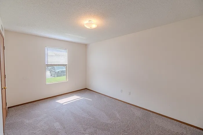 Bright bedroom at Huntley Ridge East Apartments in Springfield, MO featuring neutral walls, plush carpet, and a large window letting in natural light.