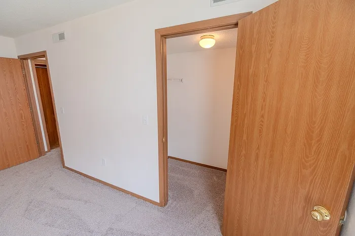 Interior view of a bedroom closet and hallway doors at Huntley Ridge East Apartments in Springfield, MO, showcasing wood trim and soft carpet throughout.