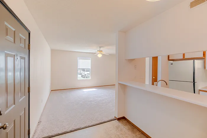 View from the entryway at Huntley Ridge East Apartments in Springfield, MO showing an open living room with plush carpet and a pass-through to the kitchen.