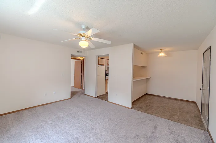 Open-concept living and dining area at Huntley Ridge East Apartments in Springfield, MO with ceiling fan, carpeted flooring, and adjacent kitchen access.