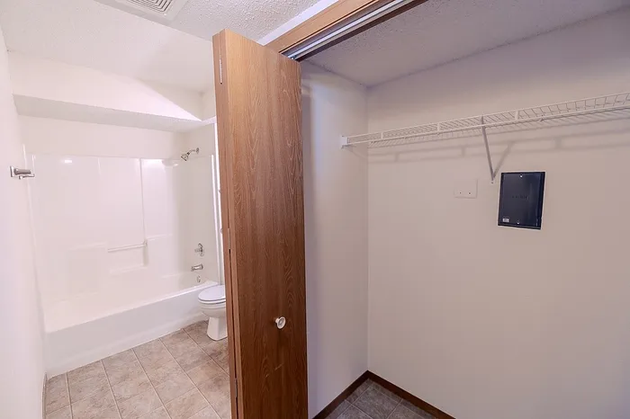 View into a full bathroom at Huntley Ridge East Apartments in Springfield, MO from the storage closet area, highlighting tile flooring, a spacious fiberglass tub, and accessible bathroom layout.