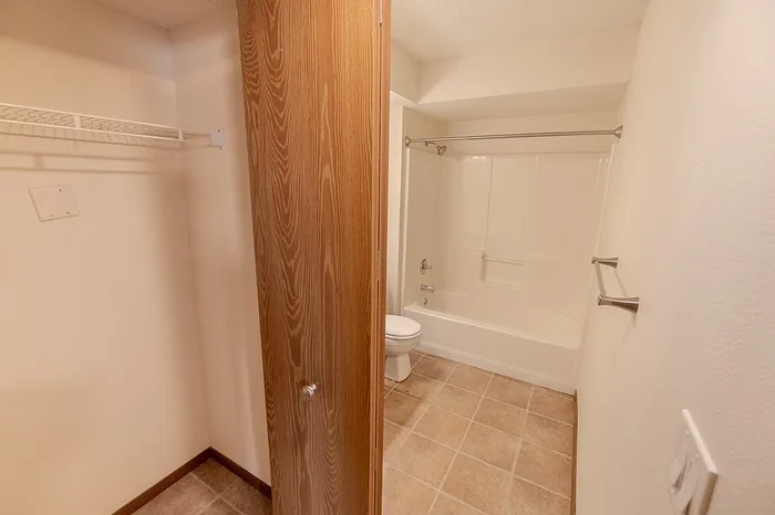 Full bathroom at Huntley Ridge East featuring a shower/tub combo, neutral tile flooring, and an in-room storage closet with built-in wire shelving&mdash;ideal for linens or essentials.