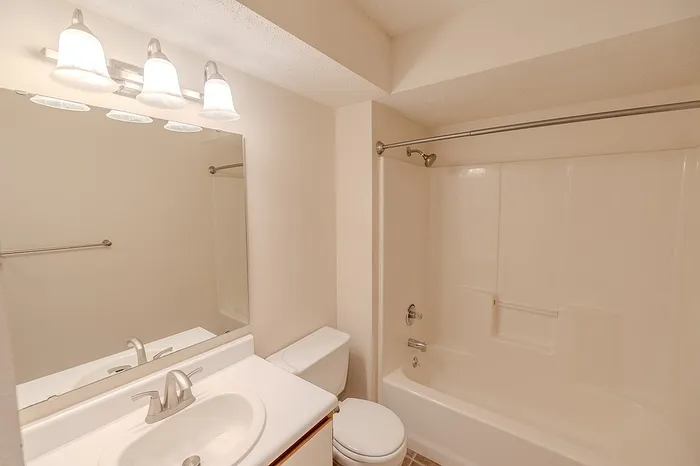 View of the 1 bathroom apartment at Huntley Ridge East, highlighting the overhead vanity lighting, large wall mirror, and tub/shower combo with curved curtain rod.