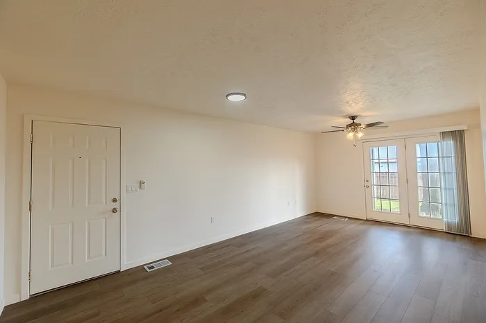 Living area featuring wood-style floors, ceiling fan with light, and French doors leading to a private outdoor space at Huntley Ridge Apartments.