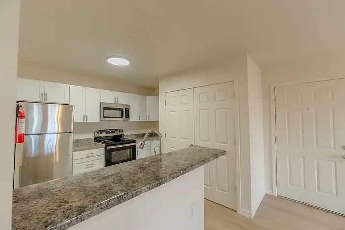 Contemporary kitchen equipped with a refrigerator, microwave, and oven, complemented by granite-look countertops and sleek white cabinets.