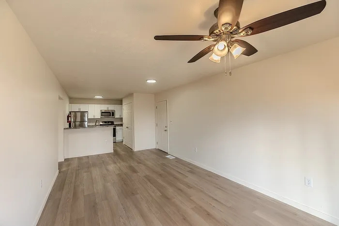 Combined living and dining area with ceiling fan, warm neutral tones, and a direct view of the upgraded kitchen and entry door.
