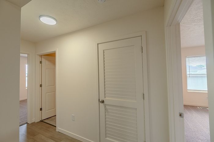 Interior hallway leading to bedrooms, featuring wood-style flooring and a vented closet door.