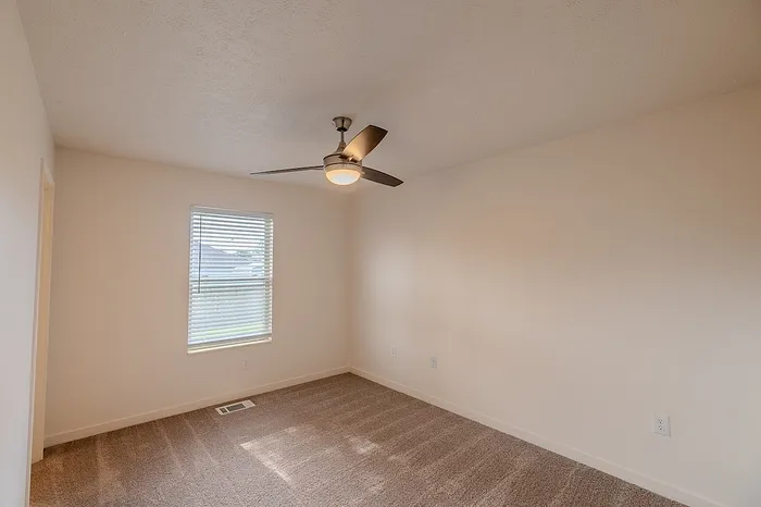 Cozy bedroom with carpet flooring, window blinds, and a modern ceiling fan with light.