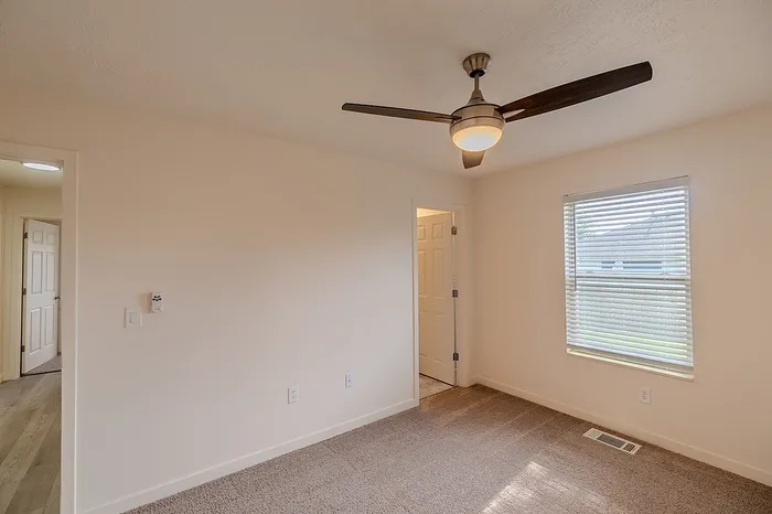 Neutral-toned bedroom at Huntley Ridge with plush carpet and sleek fan design, facing the doorway to hall.