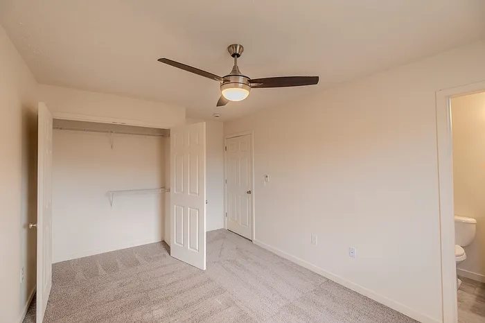 Spacious bedroom includes an open closet with shelving, direct access to bathroom, and updated light fixture.