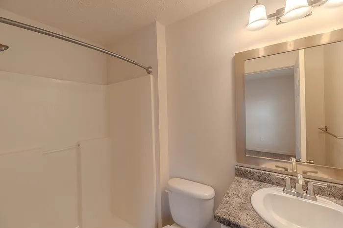 Bathroom with granite-look vanity countertop, modern lighting, and fiberglass shower unit.