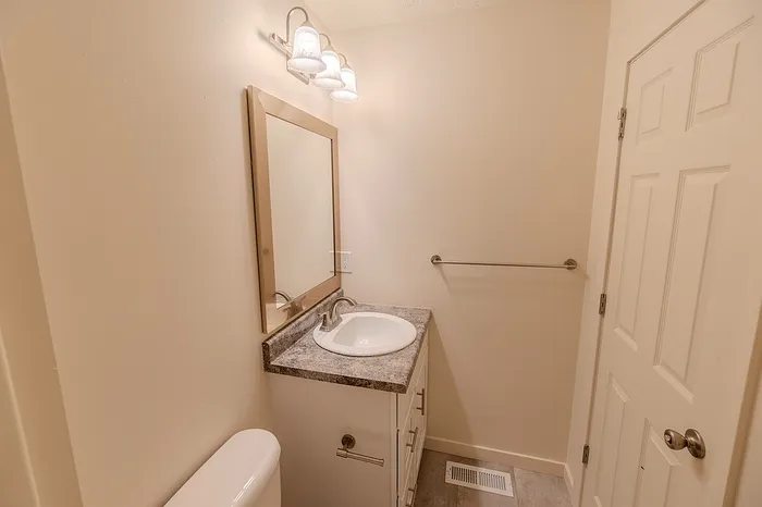 Small bathroom at Huntley Ridge featuring a white vanity with a granite-style countertop, framed mirror, and triple-light fixture.