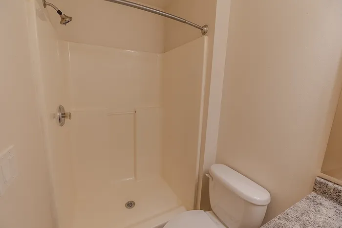 Cream-colored fiberglass shower enclosure with shelving and a modern curved shower rod in a full bathroom.