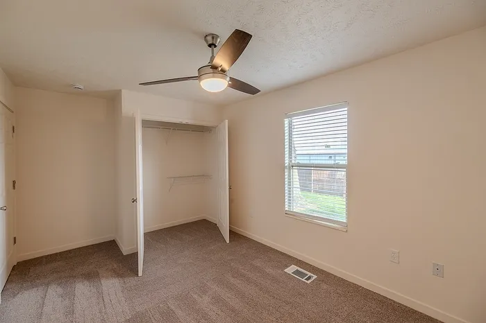 Spacious bedroom at Huntley Ridge showcasing an open double-door closet, large window, and neutral carpet flooring.