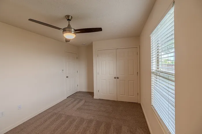 Bright bedroom with tan carpet, ceiling fan, and double-door closet offering ample storage space.
