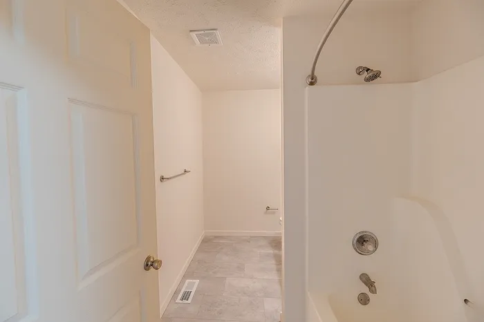 Interior shot looking out from the shower-tub combo toward the bathroom entrance, showing tile-look flooring and towel bars.