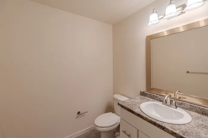 Clean and modern bathroom design at Huntley Ridge Apartments with granite-style countertop, framed mirror, and light fixture.