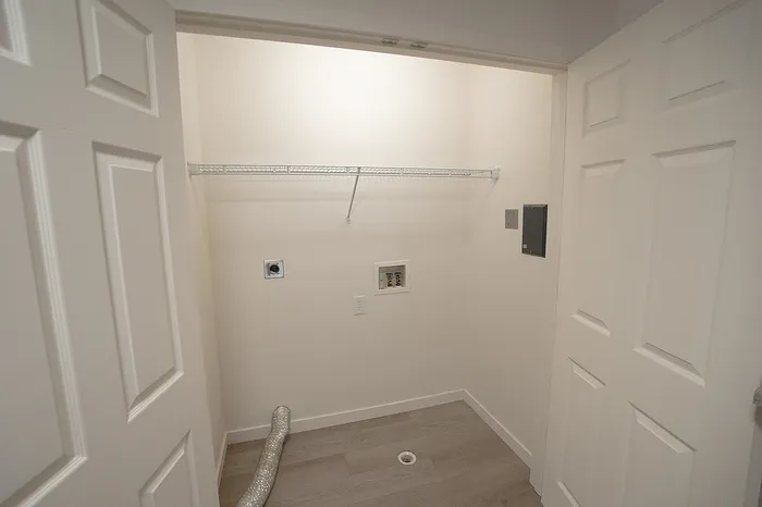 Dedicated laundry space with hookups for a washer and dryer, upper wire shelf for storage, and wood-style flooring.