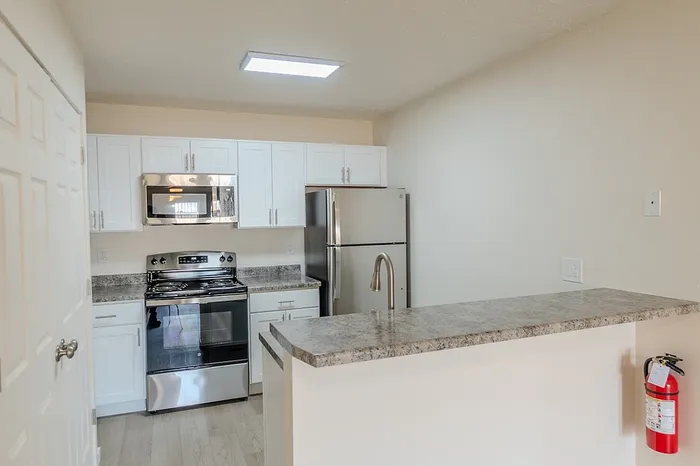Modern kitchen featuring stainless steel appliances, white shaker cabinets, and faux granite countertops in a 1-bedroom renovated apartment in Battlefield, MO.