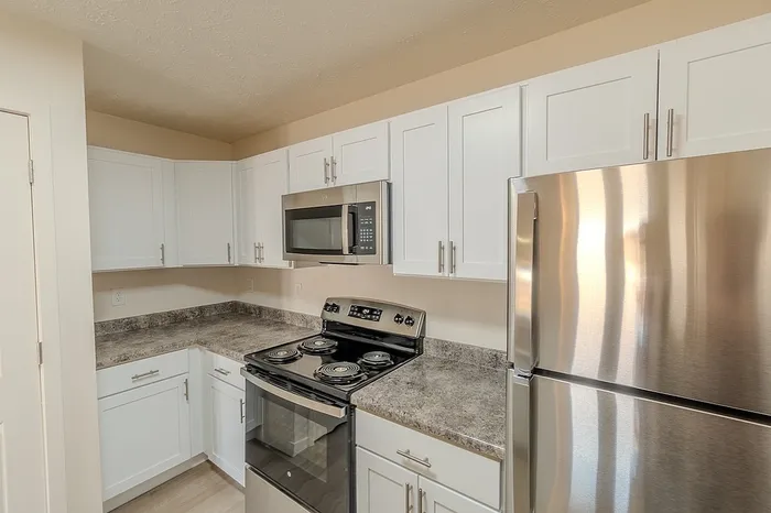 Close-up of updated kitchen cabinetry and countertops with stainless range, microwave, and refrigerator in Battlefield, MO apartment.